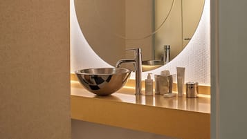 A bathroom with a round mirror, a bowl sink, and toiletries on the counter.