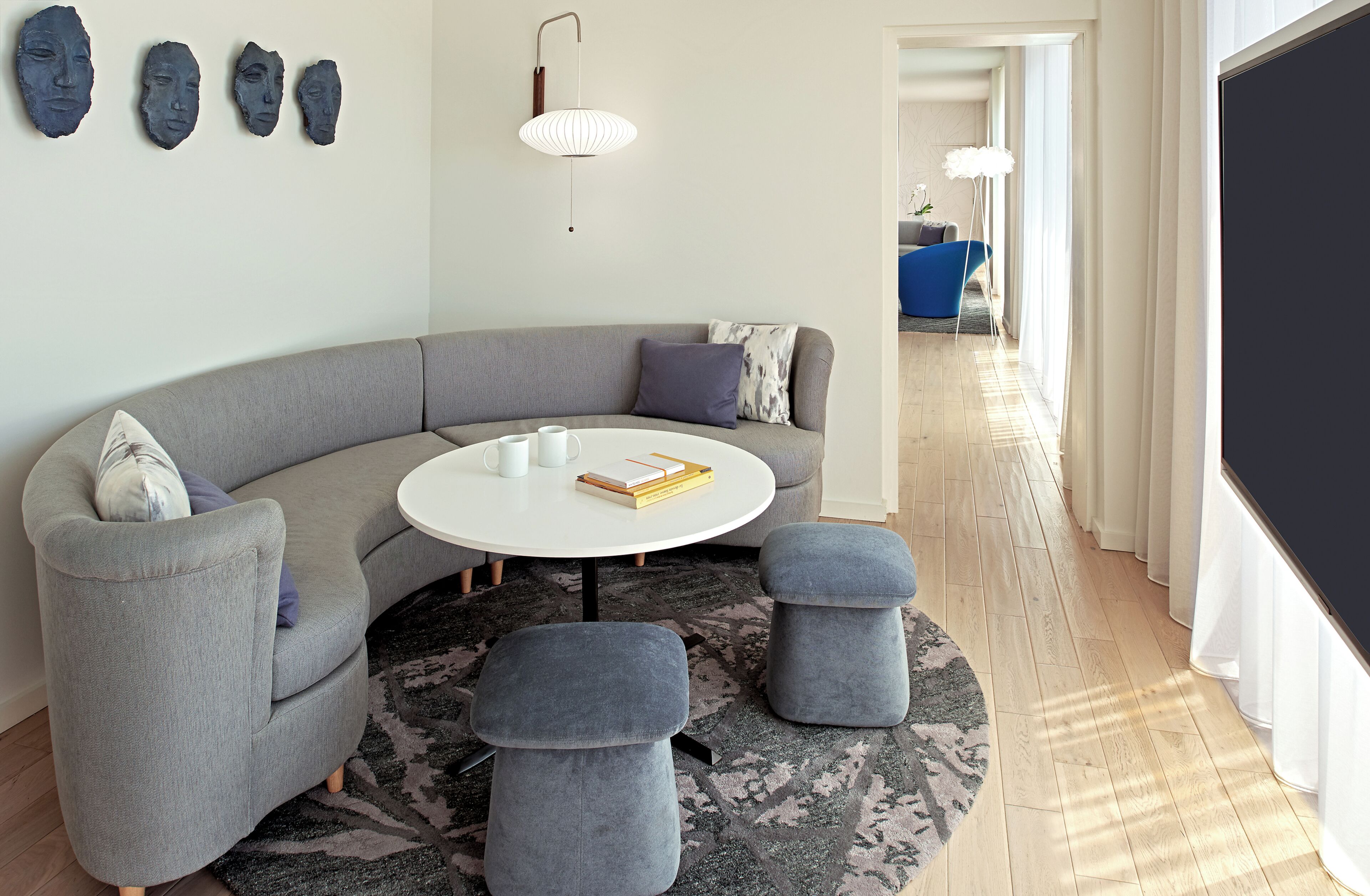 A modern living room with a grey sofa, round coffee table, and ottomans, a white lamp, and abstract wall art.