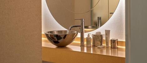 Un baño moderno con un espejo redondo, un lavabo de acero inoxidable y artículos de aseo en la encimera.