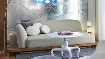 A modern living room with a sofa, ottoman, and chairs, a glass wall with a crack pattern, and a blue pendant light.