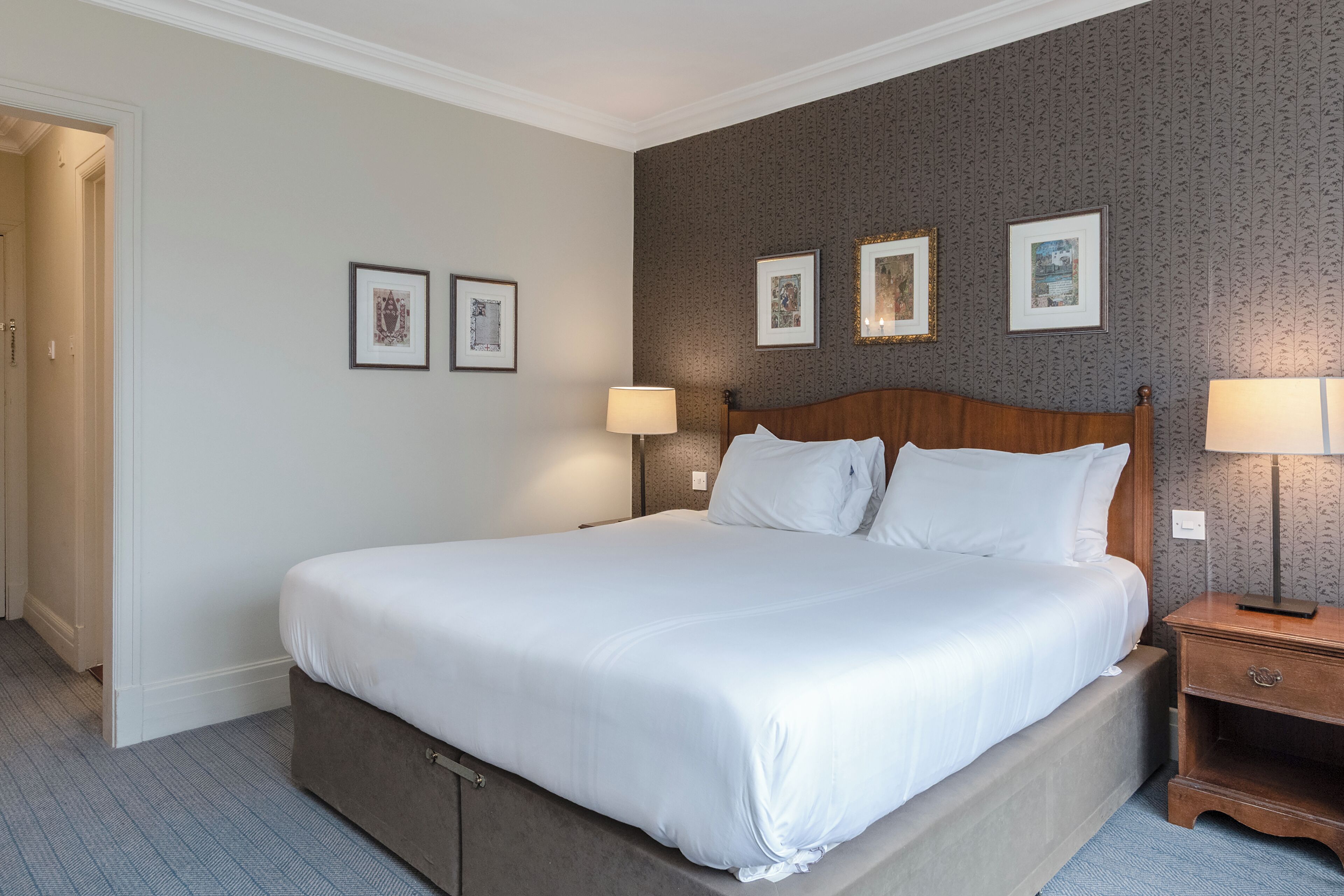 A neatly made bed with white linens, a wooden headboard, and a nightstand with a lamp.