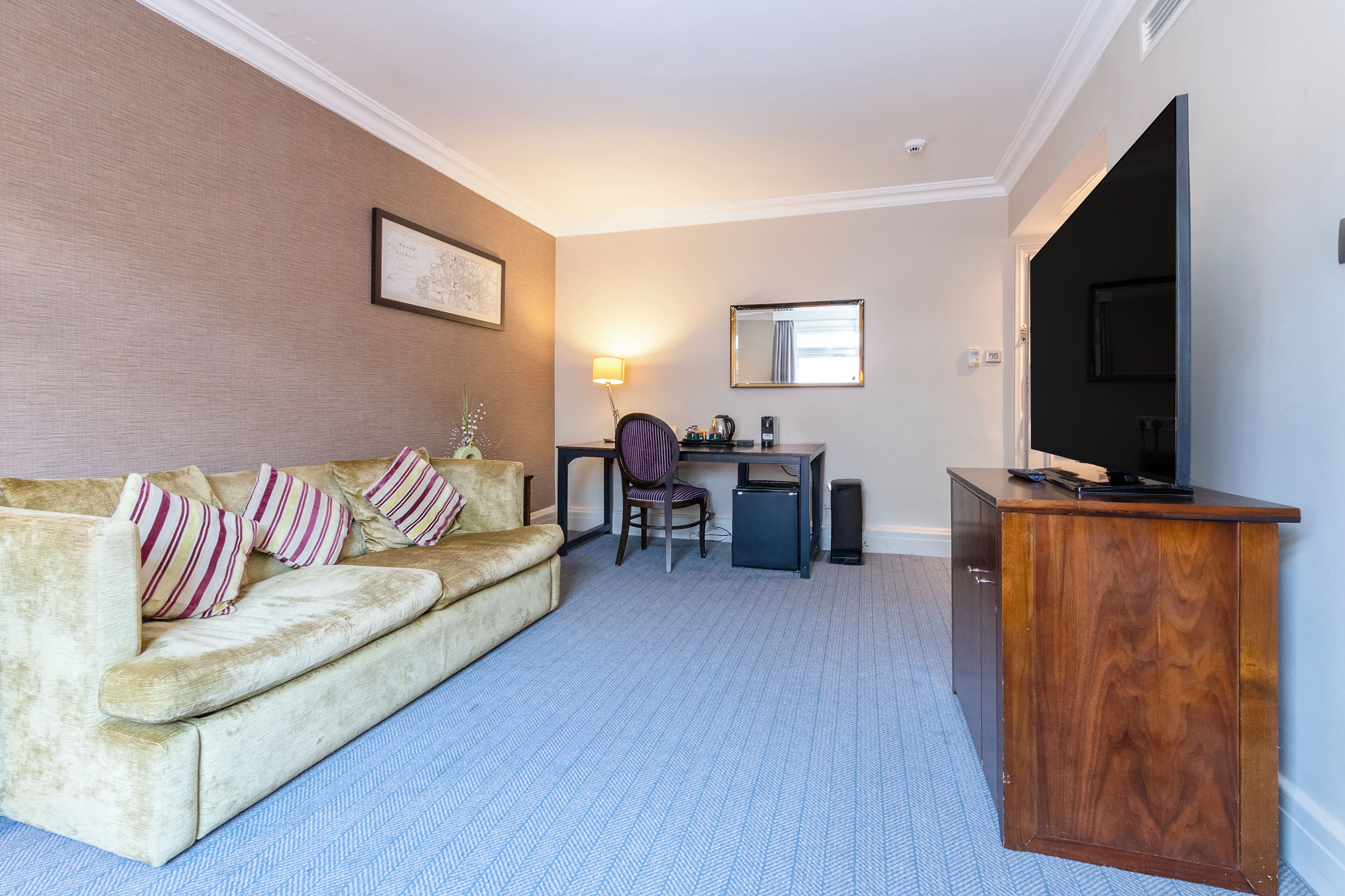 Una habitación de hotel con sofá, escritorio, silla, televisor y un mueble pequeño.