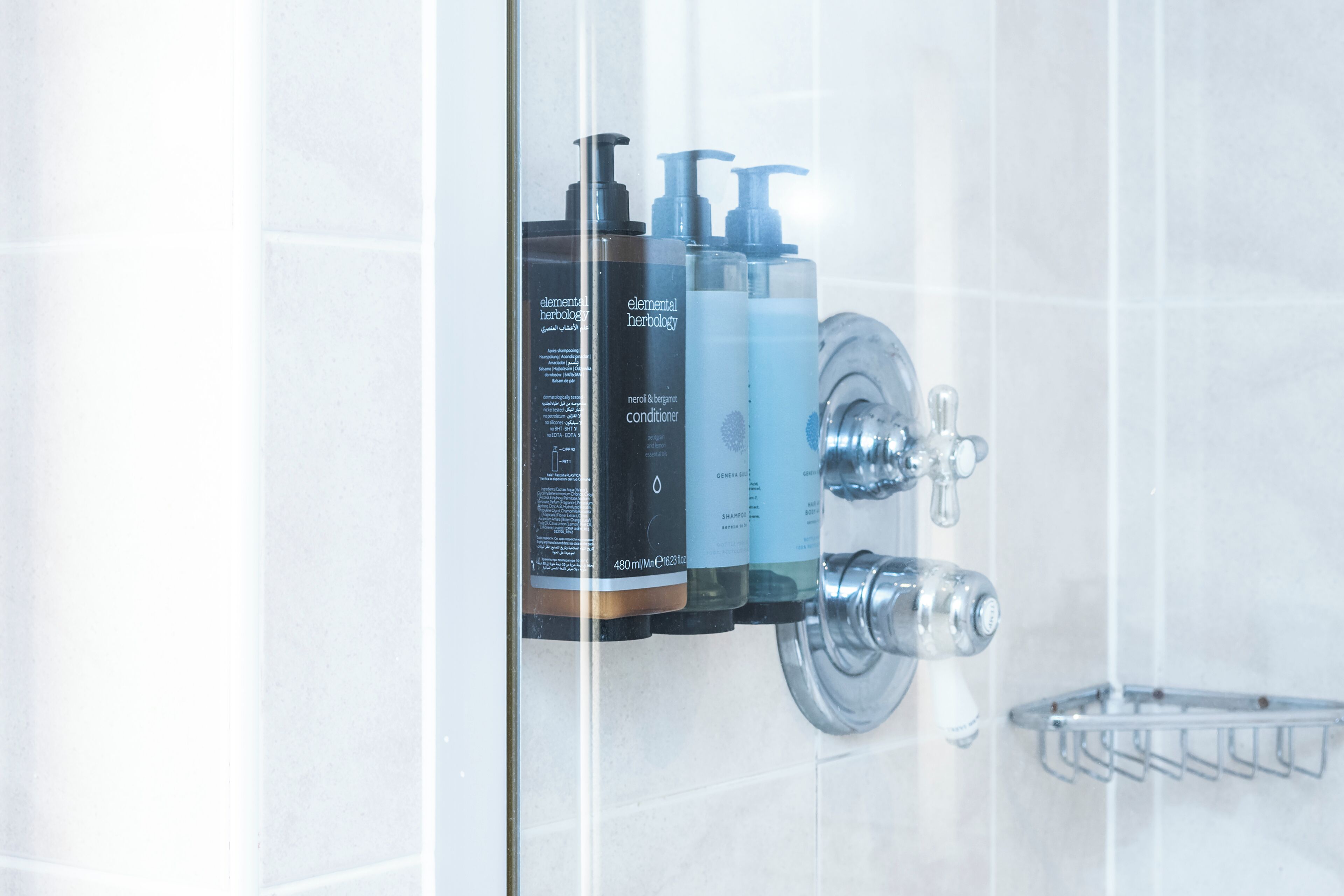 Une salle de bain avec une douche à parois de verre, un robinet chromé et trois flacons de produits de toilette fixés au mur.