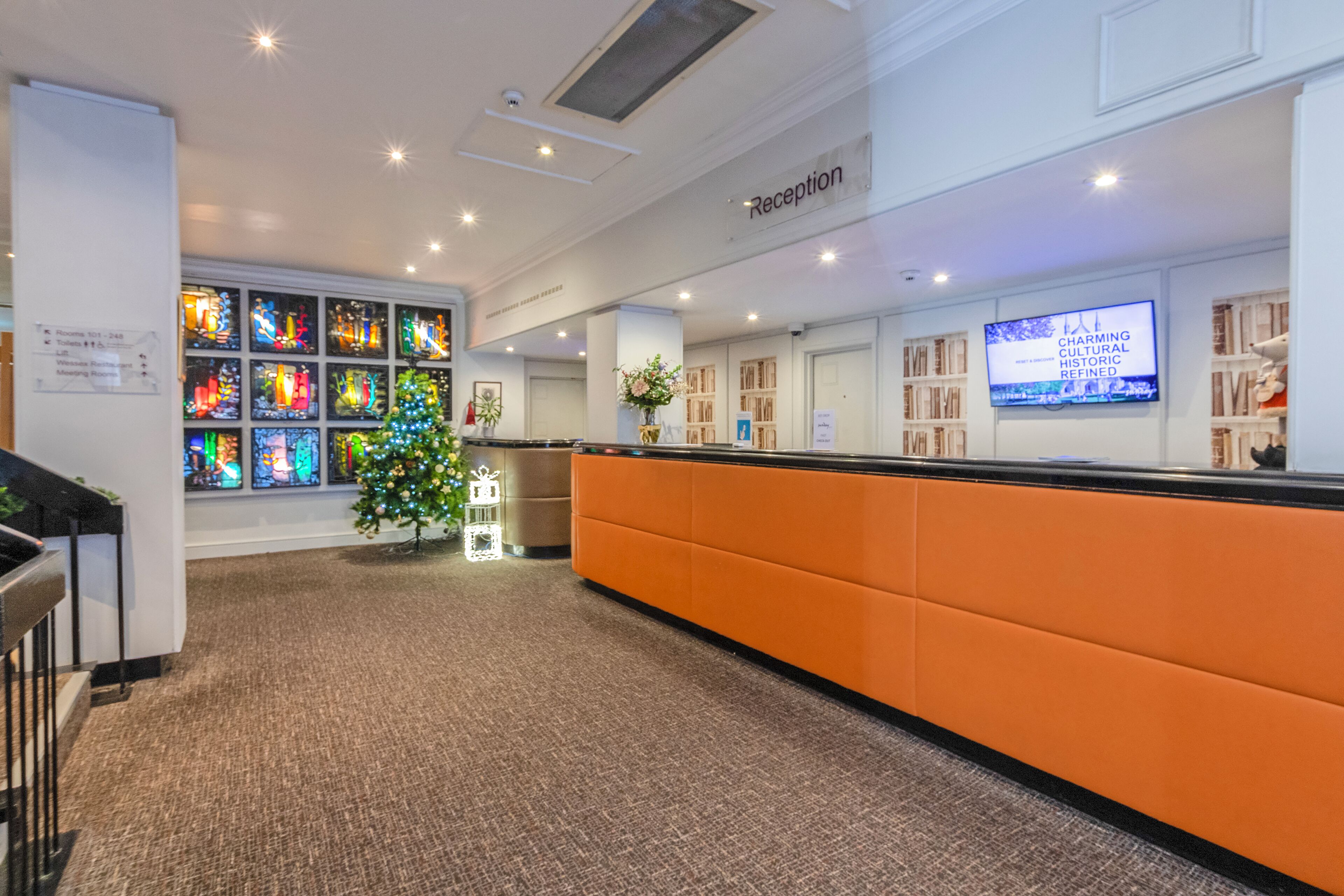 A reception area with a modern design, featuring a reception desk, a Christmas tree, and a large digital display.