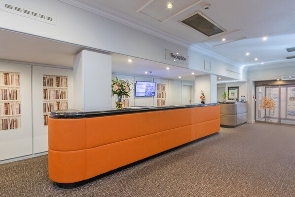A reception area with a reception desk, a television screen, and a bookshelf.