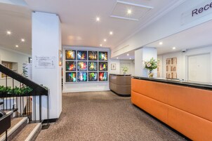 Zona de recepción con mostrador, escalera y pared con vidrieras de colores.