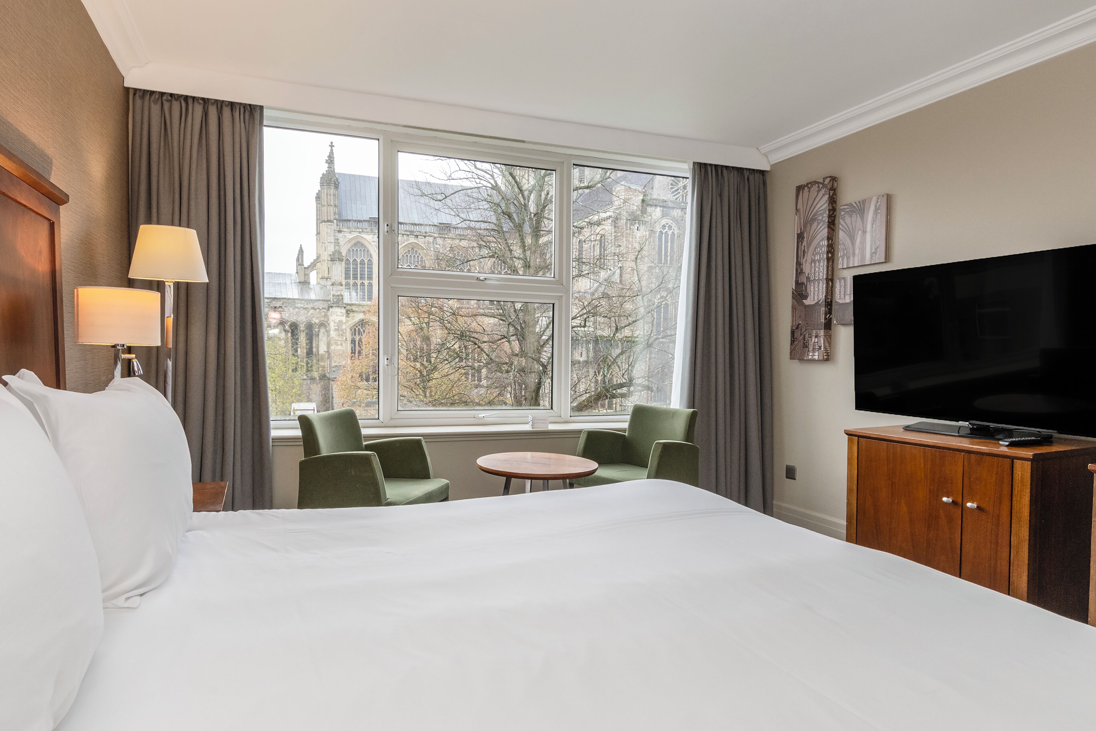 A hotel room with a large bed, a television, a small table, two chairs, and a view of a historic building through the window.