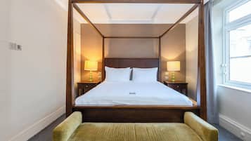 A four-poster bed with a wooden frame, two bedside lamps, and a small green armchair.