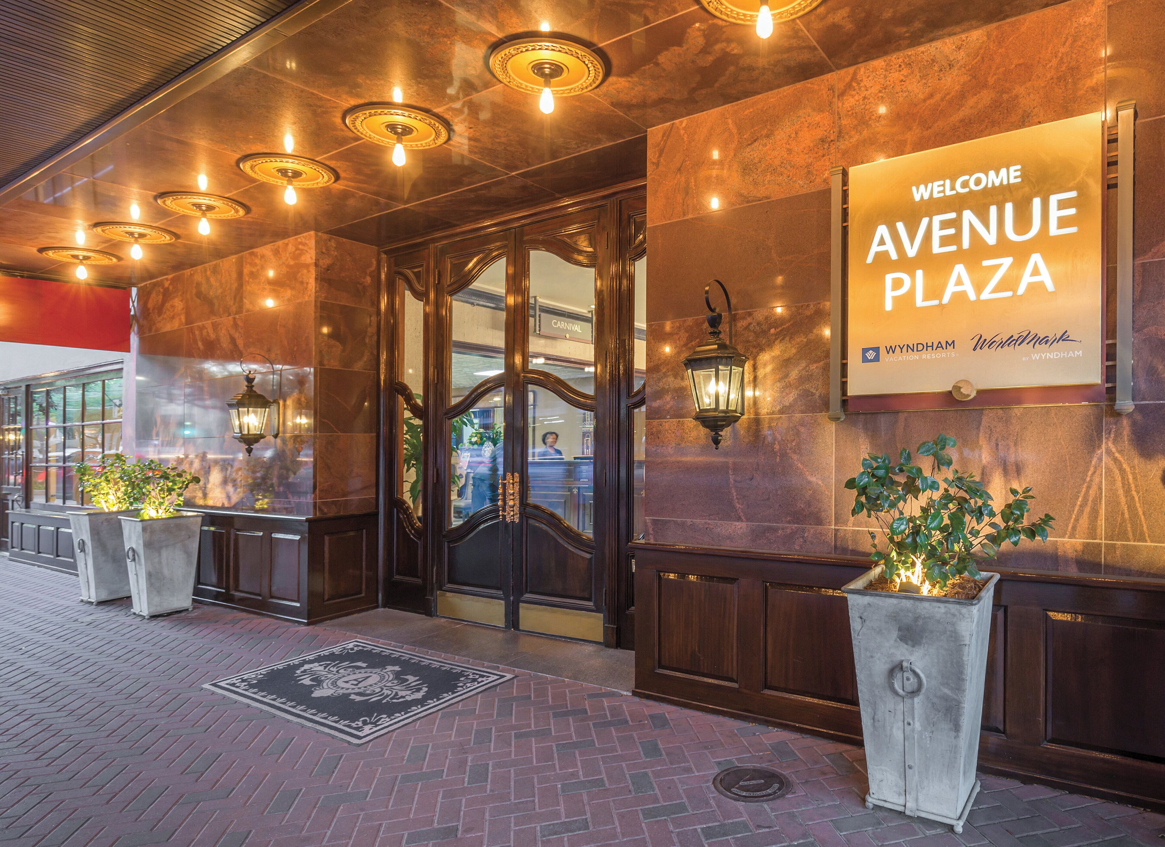 Entrada de hotel con un cartel que dice 'Welcome Avenue Plaza', una puerta de cristal y un área de acceso empaveda con ladrillos.