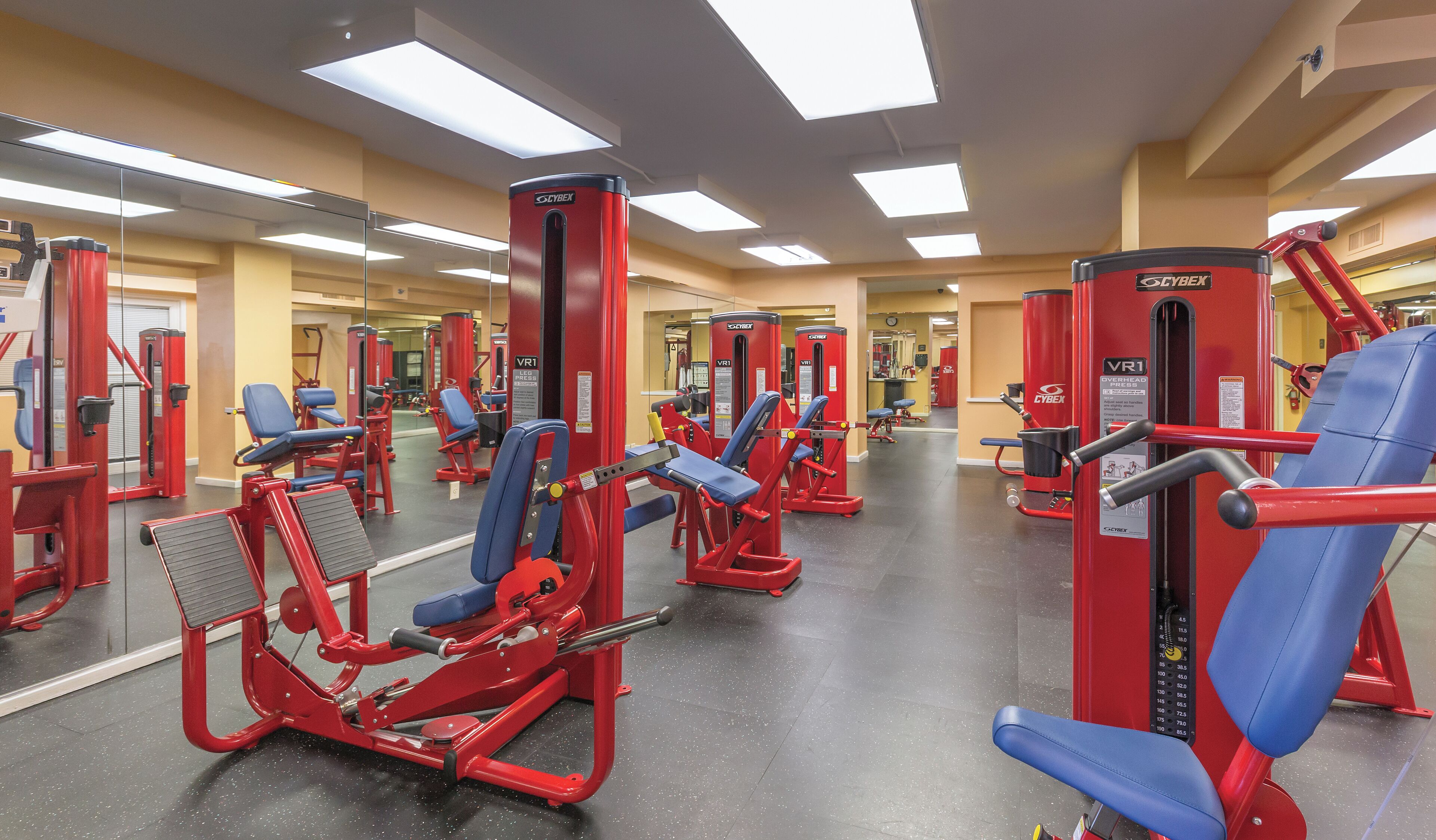 A gym with red and blue exercise equipment, mirrors on the walls, and a tiled floor.