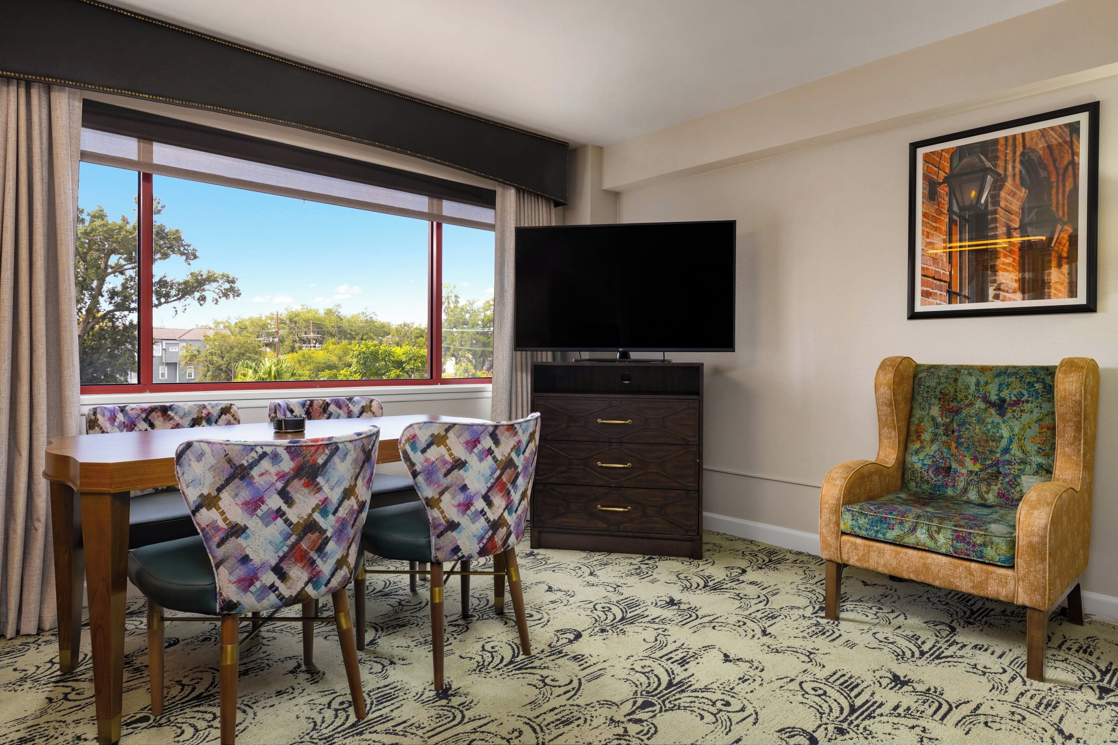A room with a dining table, chairs, a TV, a chair, and a patterned carpet.