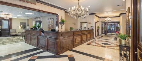 A hotel lobby with a reception desk, a chandelier, and a check-in counter.