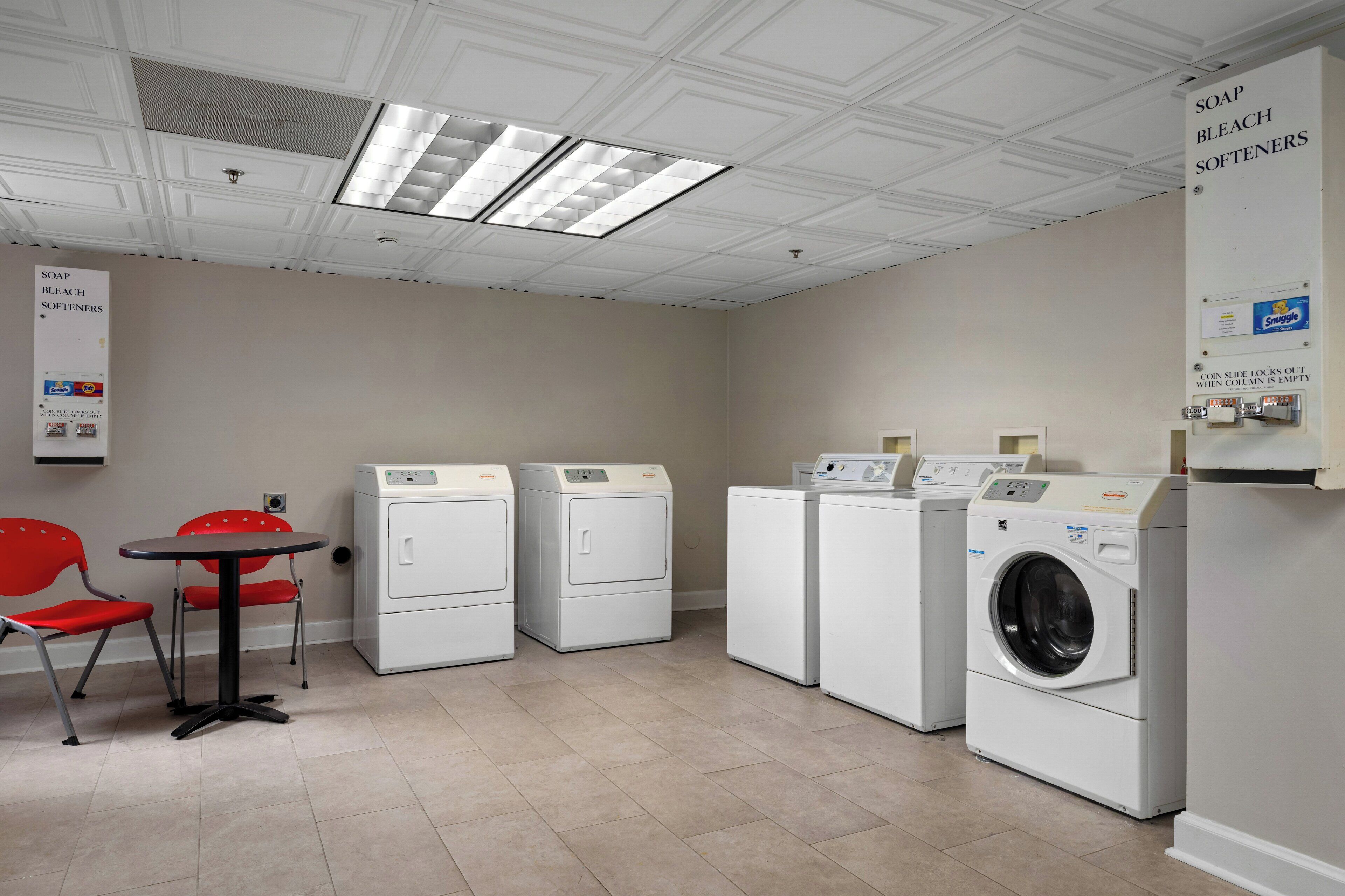 A laundry room with four washing machines, a table with chairs, and a sign indicating soap, bleach, and softeners.