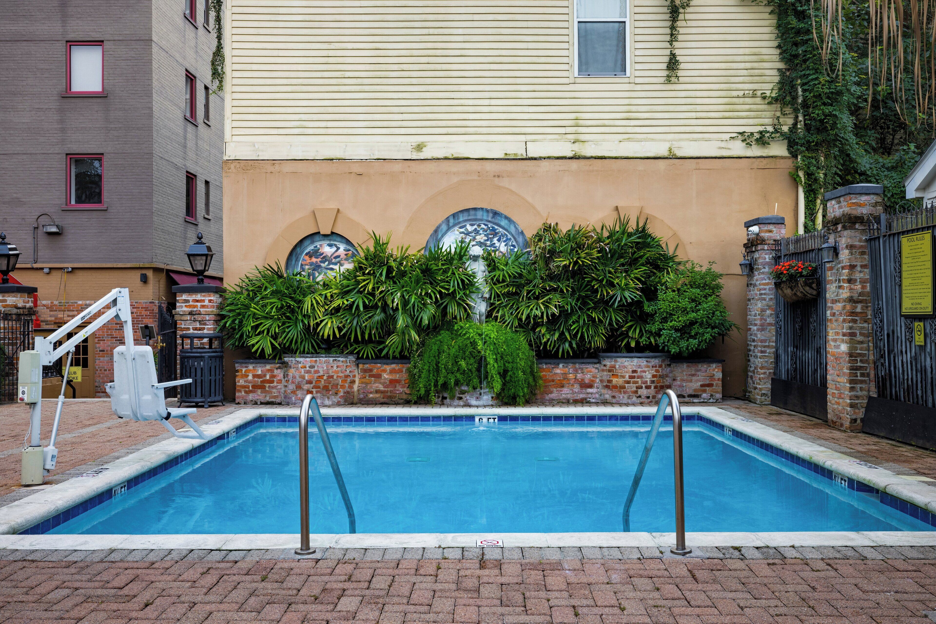 A swimming pool with a brick border, surrounded by a brick wall and potted plants.
