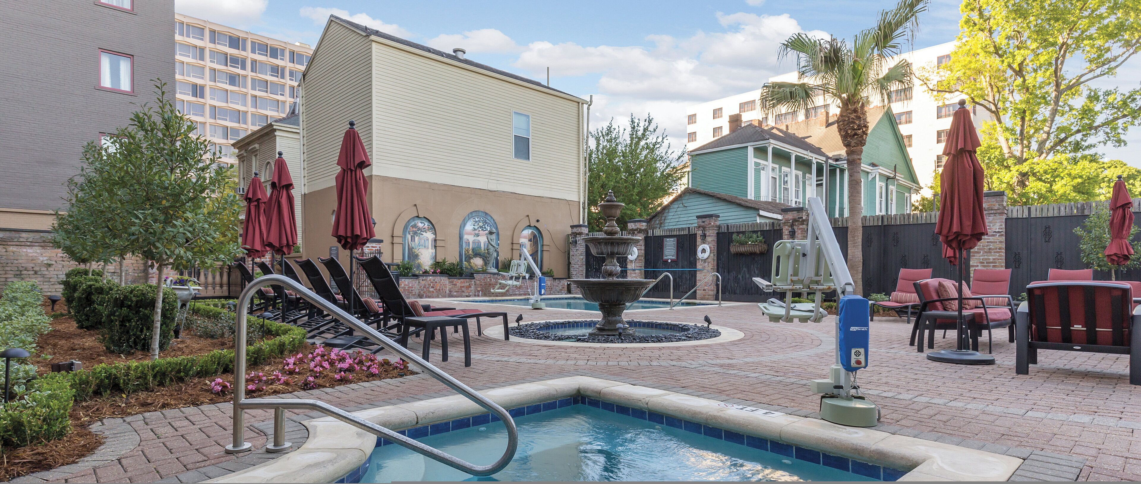 A pool area with a fountain, lounge chairs, and umbrellas.