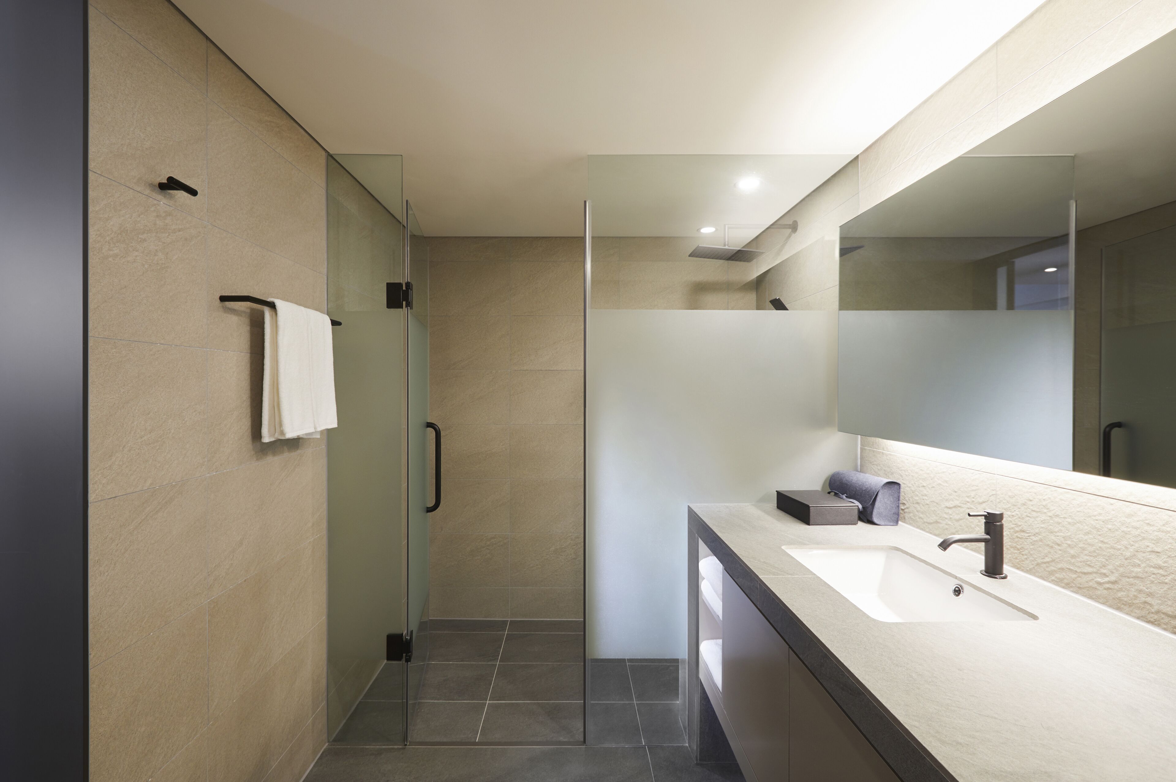 A modern bathroom with a glass shower enclosure, a large mirror, and a countertop with a sink and towel rack.