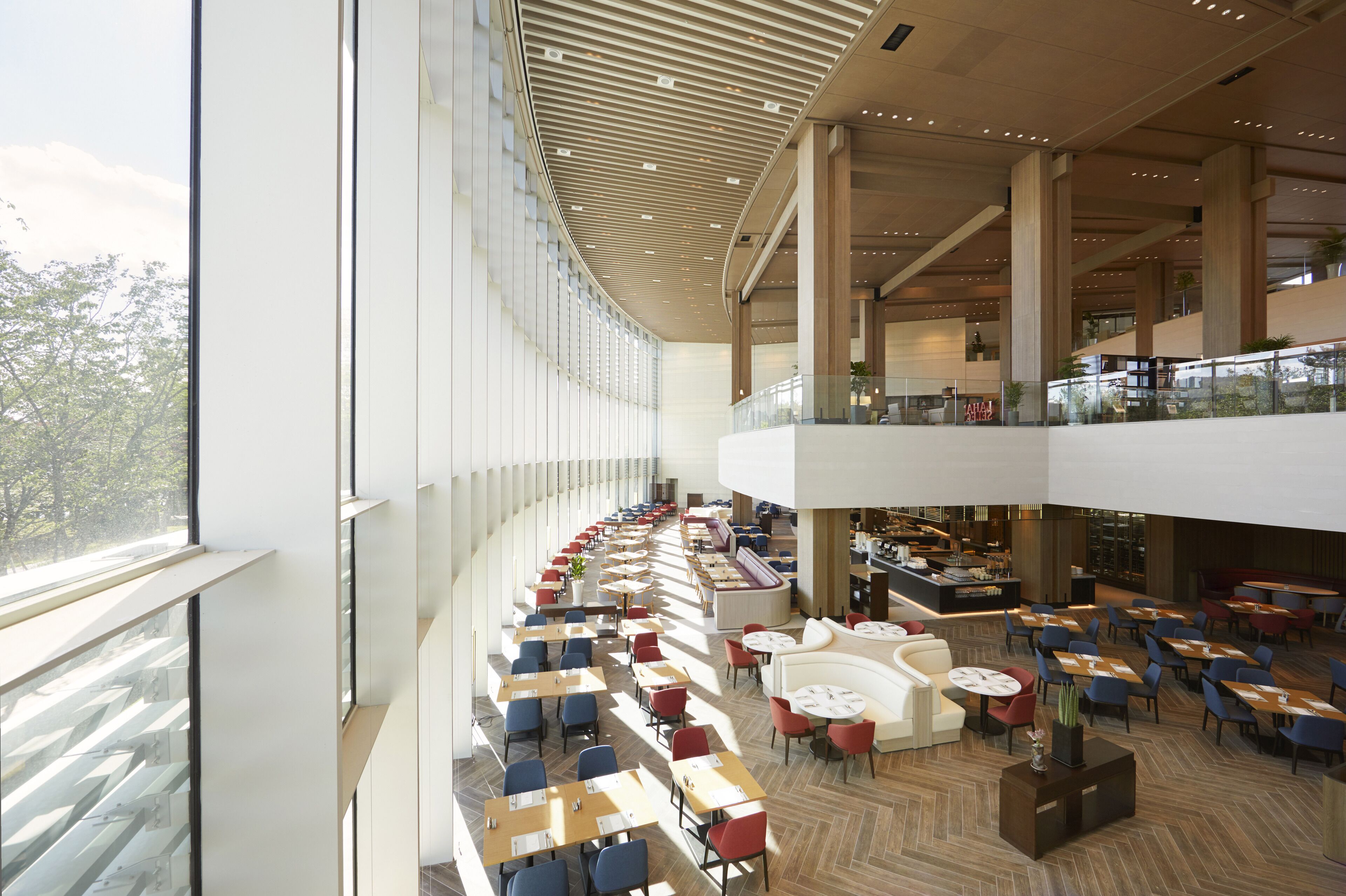 Un ampio spazio interno con diversi tavoli e sedie da pranzo, una zona salotto centrale con divani e un soffitto alto dal design moderno.