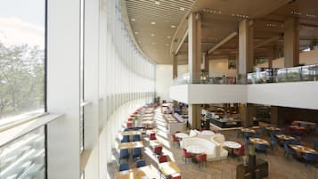Un ampio spazio interno con diversi tavoli e sedie da pranzo, una zona salotto centrale con divani e un soffitto alto dal design moderno.