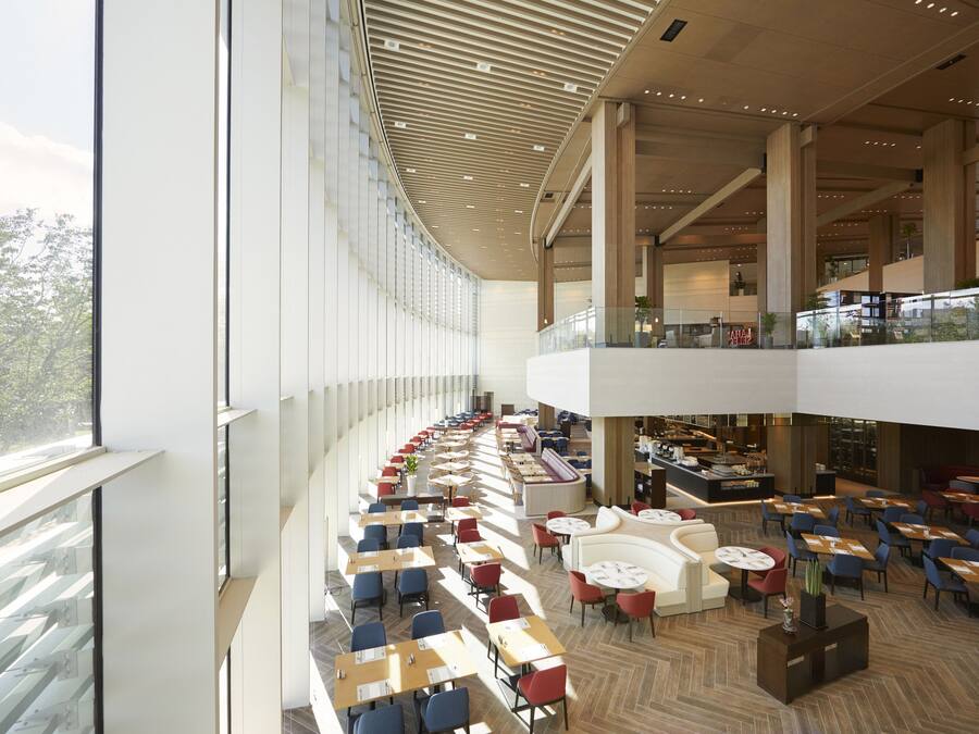 Un ampio spazio interno con diversi tavoli e sedie da pranzo, una zona salotto centrale con divani e un soffitto alto dal design moderno.