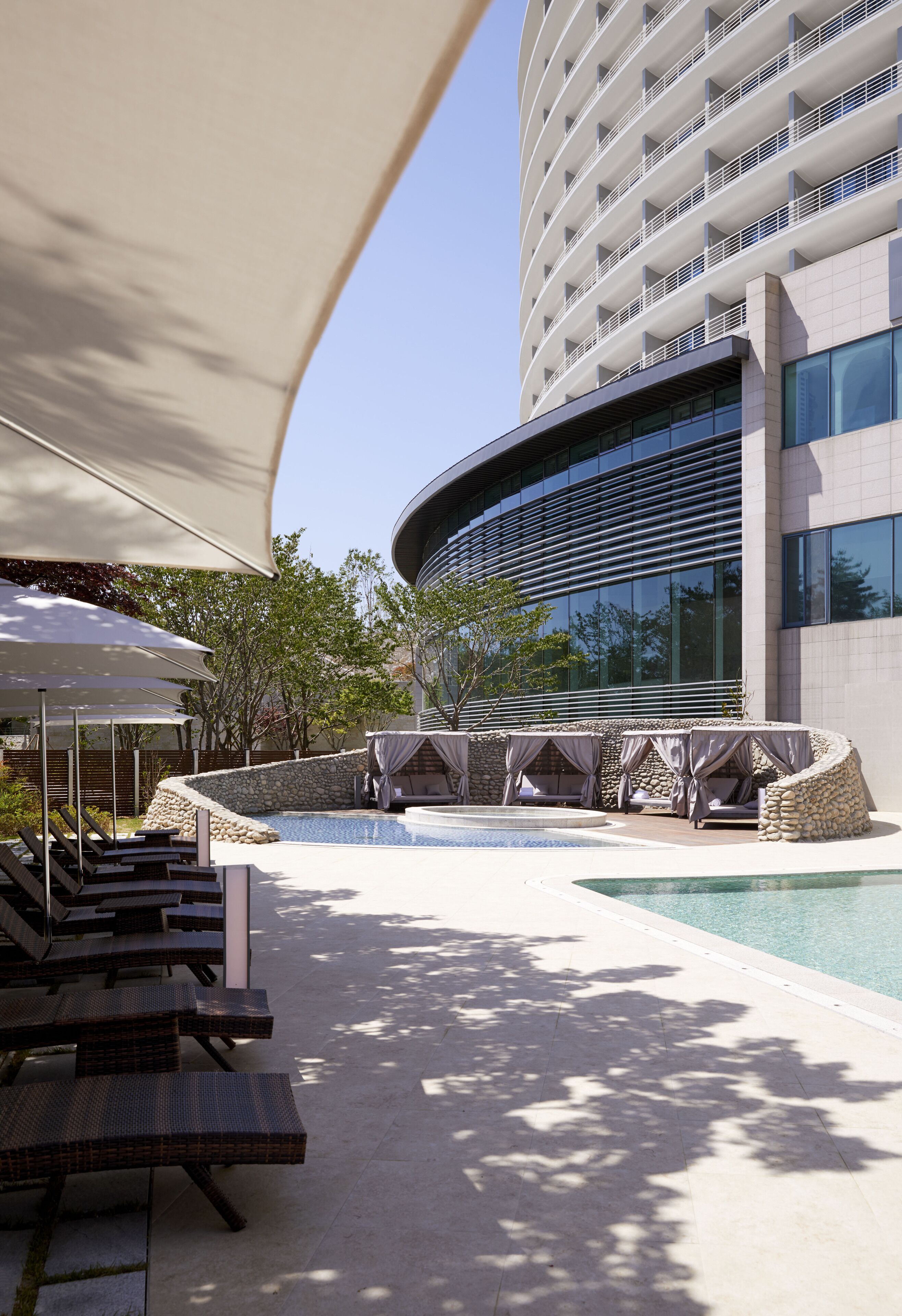A modern hotel with a swimming pool, outdoor seating, and a large building with balconies.