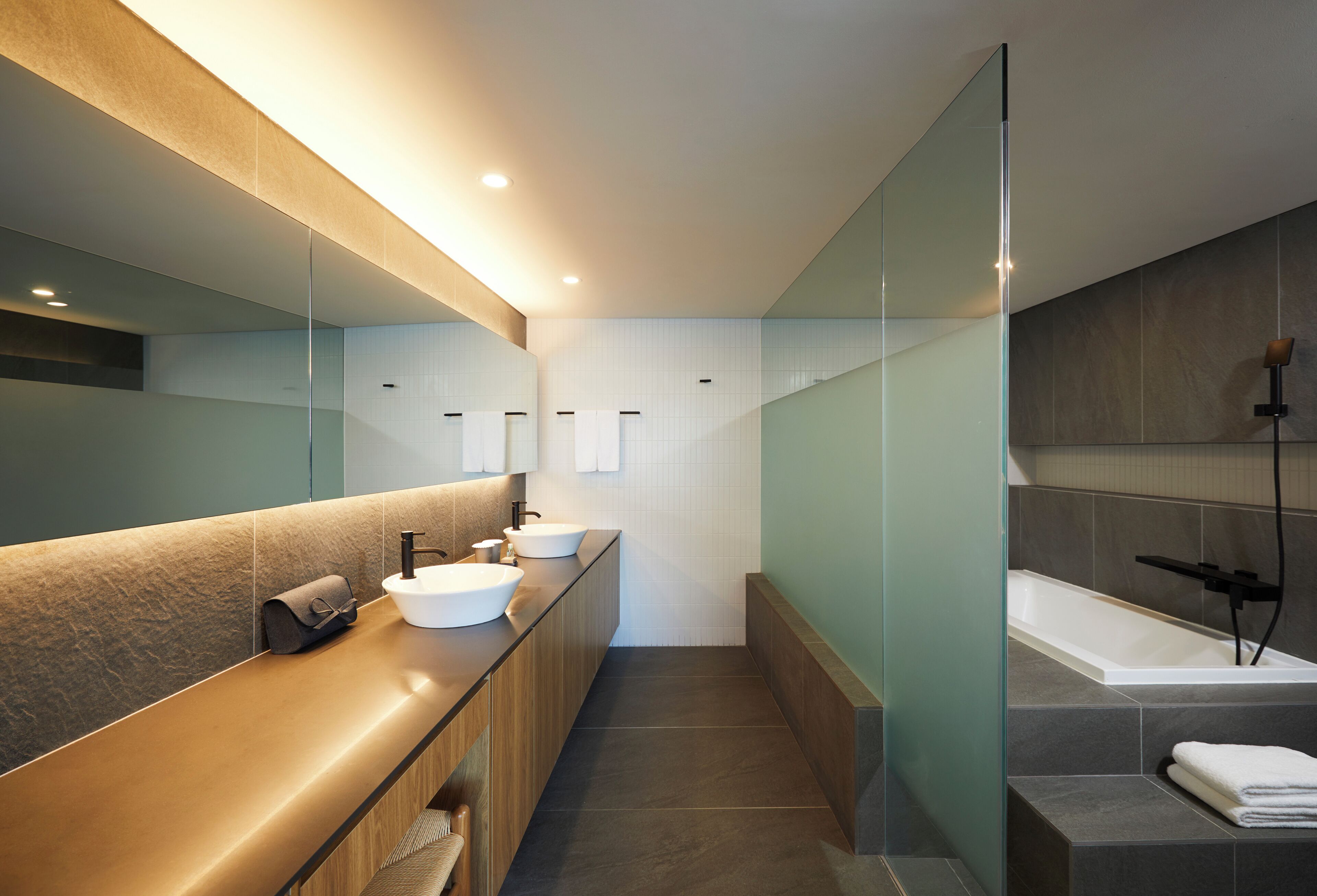 A modern bathroom with a long vanity, a large mirror, a bathtub, and a glass shower enclosure.