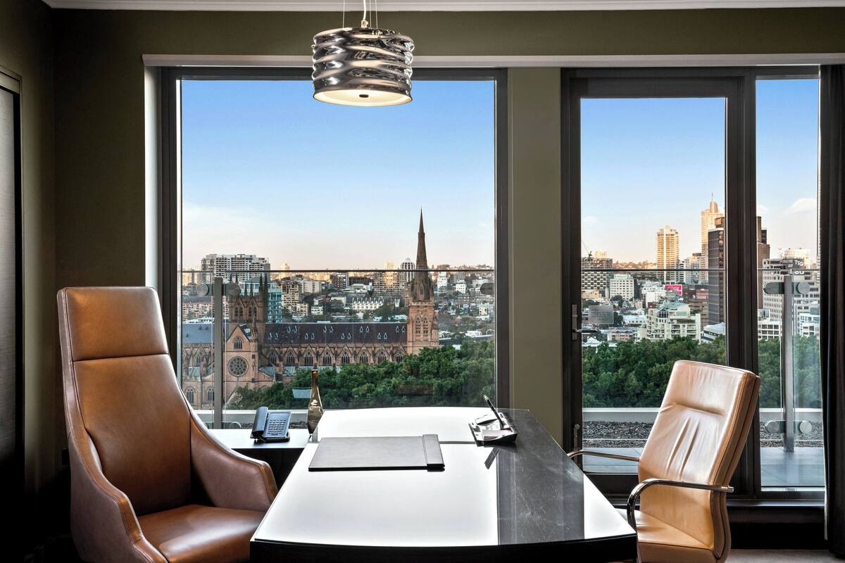 Een modern kantoor met twee lederen stoelen, een bureau en uitzicht op een stadsbeeld met een opvallende kerktoren.