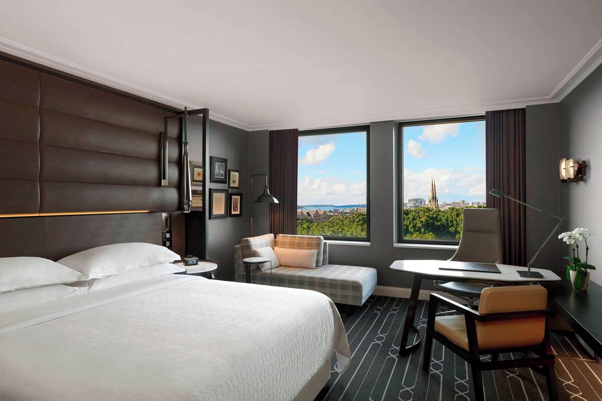 Een hotelkamer met een groot bed, een bureau, een stoel en uitzicht op een stadsbeeld.