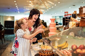 A buffet with various food items and a woman and a child selecting food. - Sheraton Grand Sydney Hyde Park (Sydney)