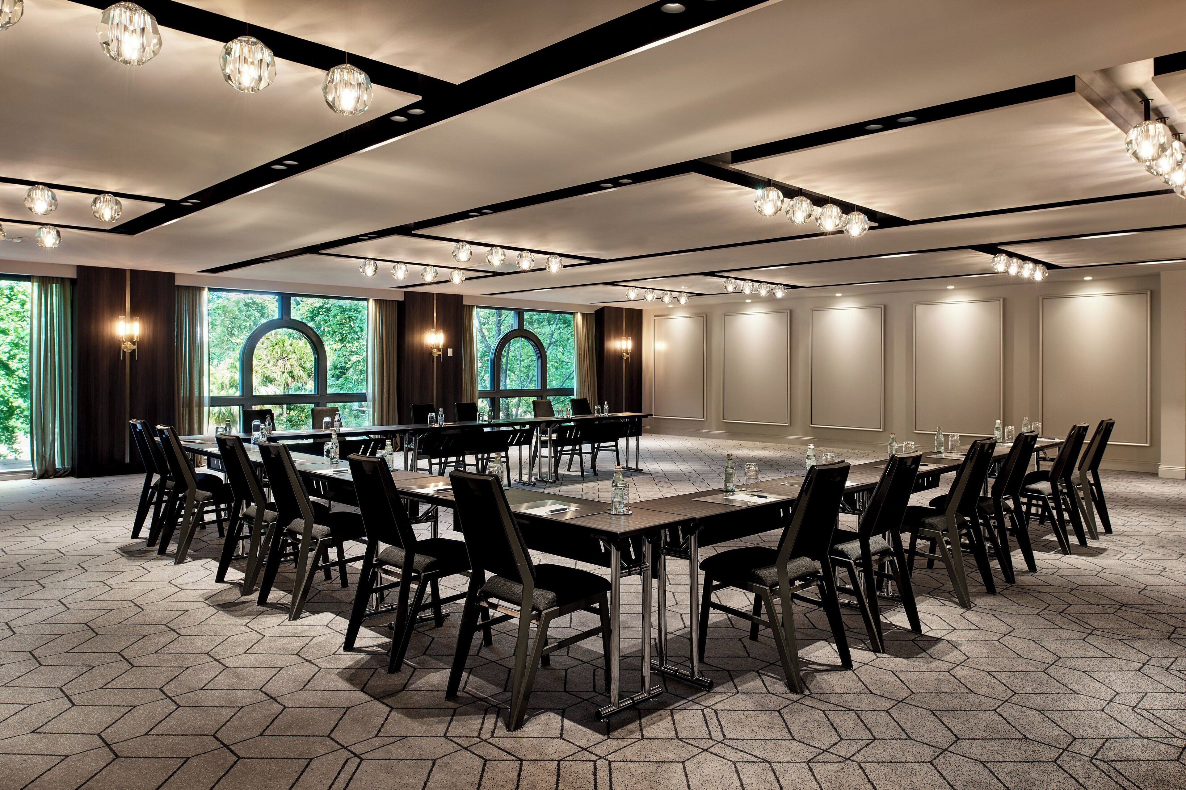 A conference room with hexagonal patterned flooring, multiple tables and chairs, and large windows with a view of greenery.