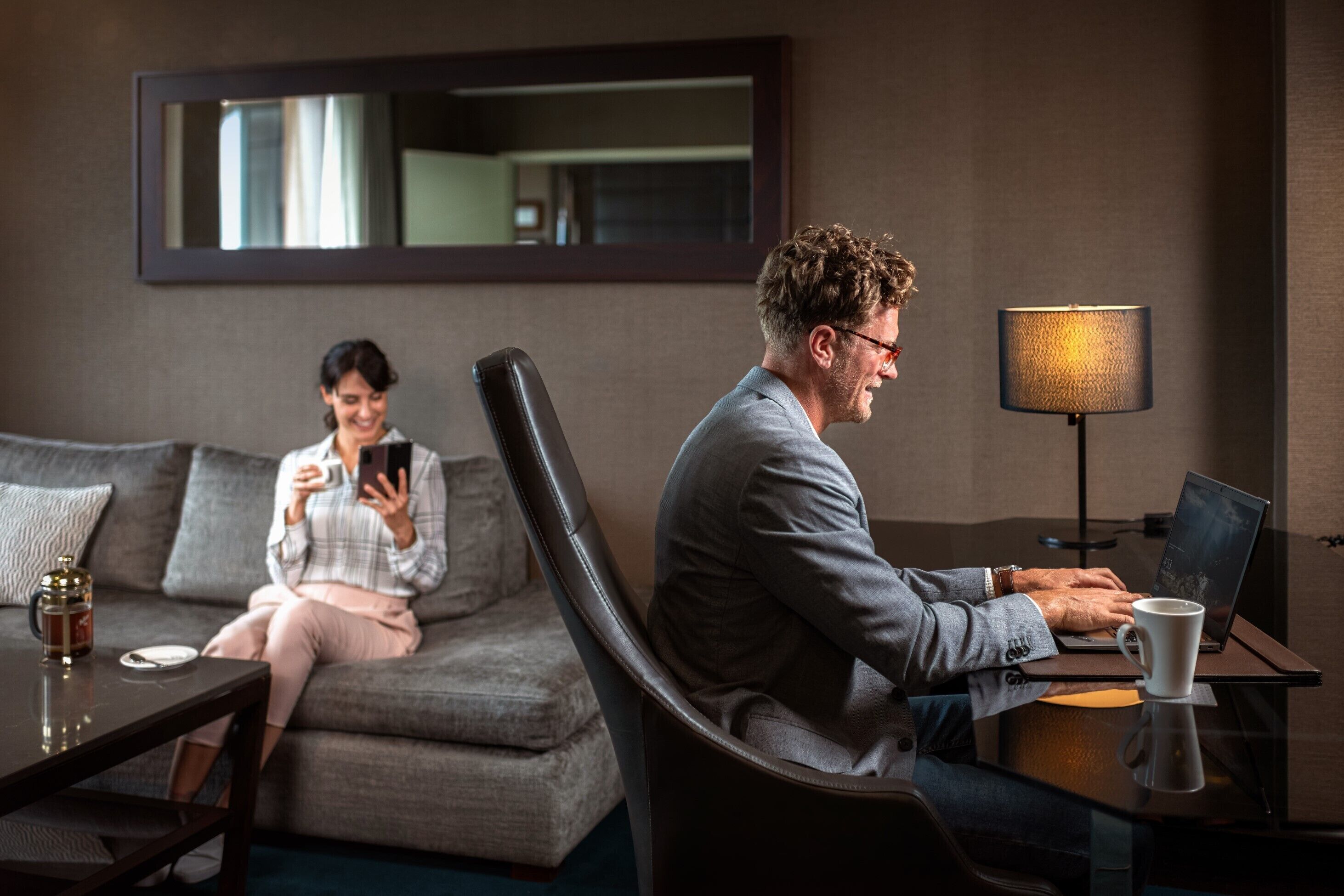 A man working on a laptop in a modern hotel room with a sofa and a coffee table.
