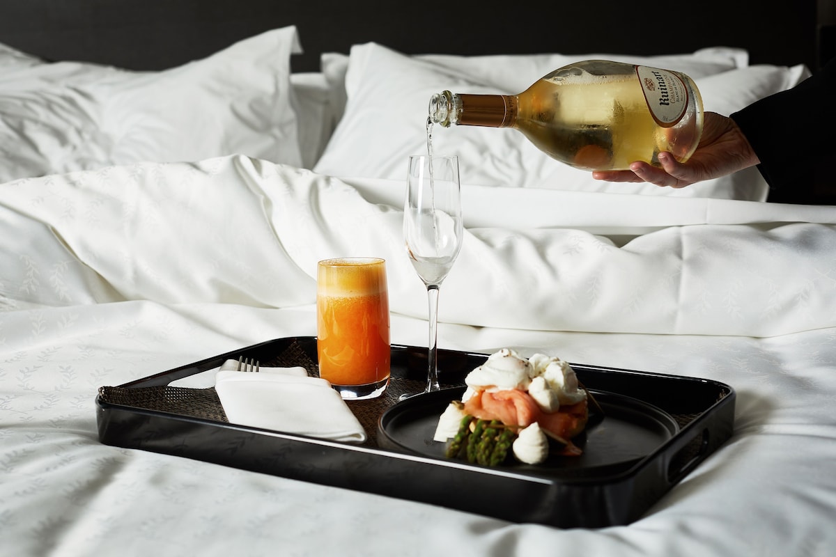 A tray with food and a glass of orange juice on a bed.