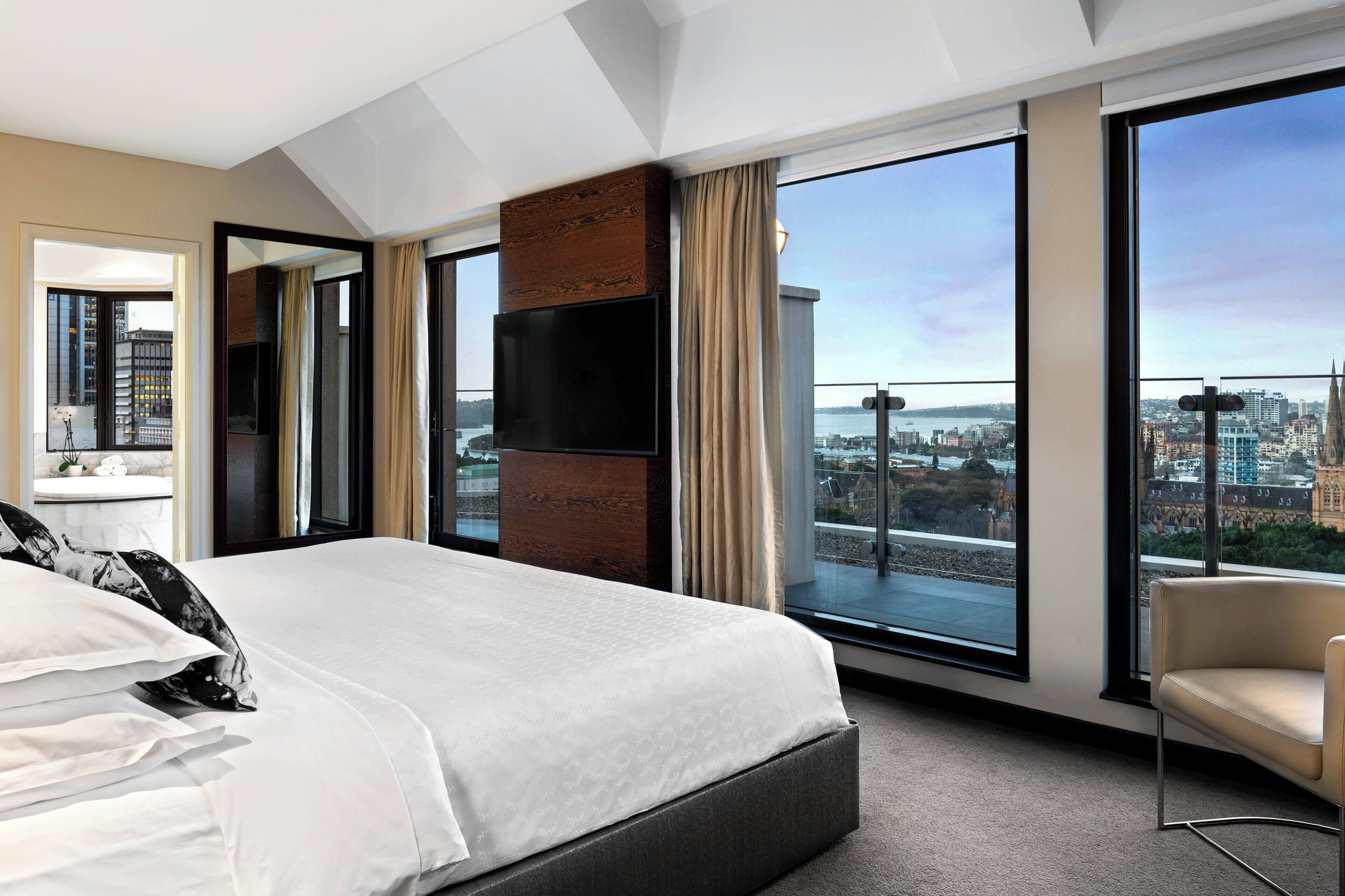 Ein modernes Hotelzimmer mit einem großen Bett, einem Fernseher und einem Balkon mit Blick auf die Stadt.