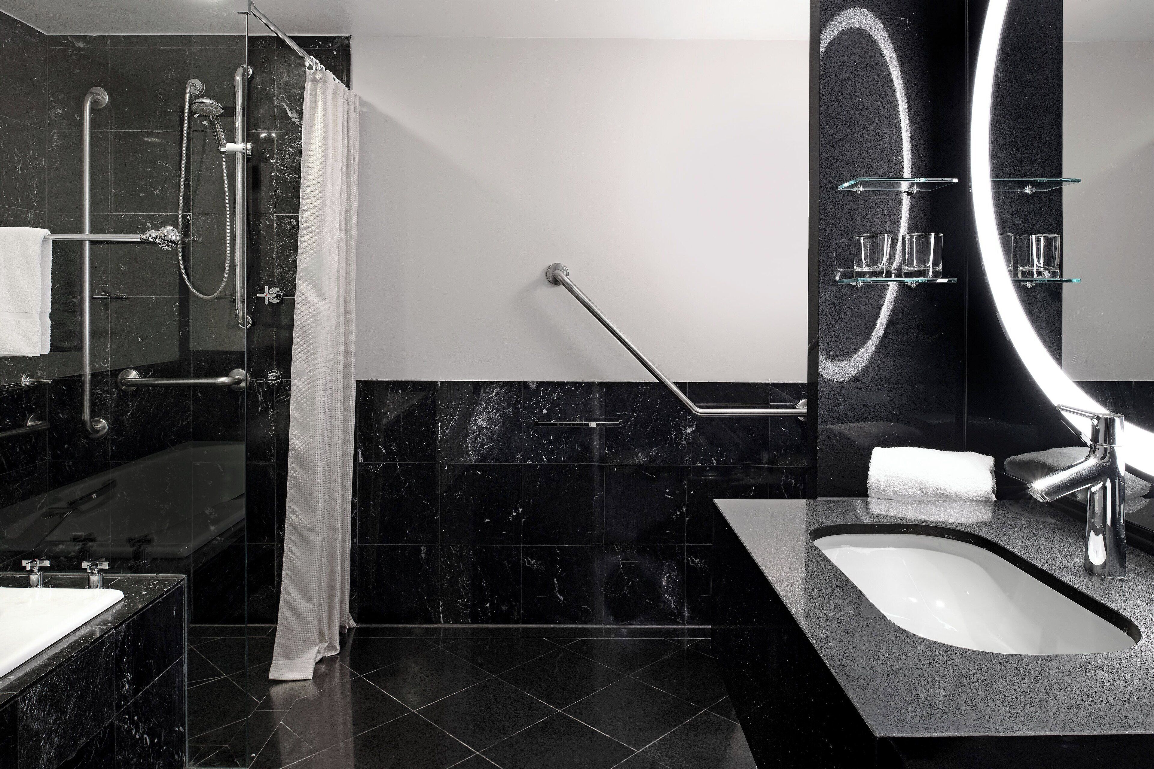Un bagno moderno con cabina doccia in vetro, una vasca da bagno freestanding, un mobile lavabo e un grande specchio con illuminazione circolare.
