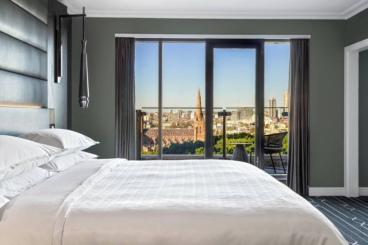 Hotelkamer met een groot bed, stadszicht en een balkon met een stoel.