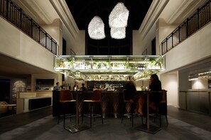 A bar area with a high ceiling, hanging pendant lights, and a bar counter with stools.