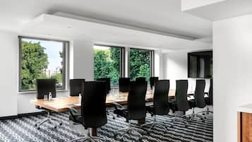 A conference room with a large table, black chairs, and large windows offering a view of trees and buildings.