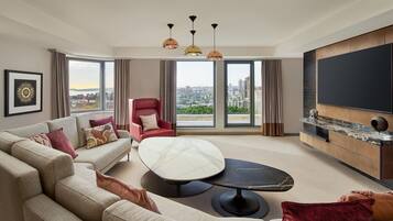 Un salon moderne avec un canapé, un fauteuil et une table basse ronde. Un grand téléviseur est fixé au mur et les fenêtres offrent une vue sur la ville.