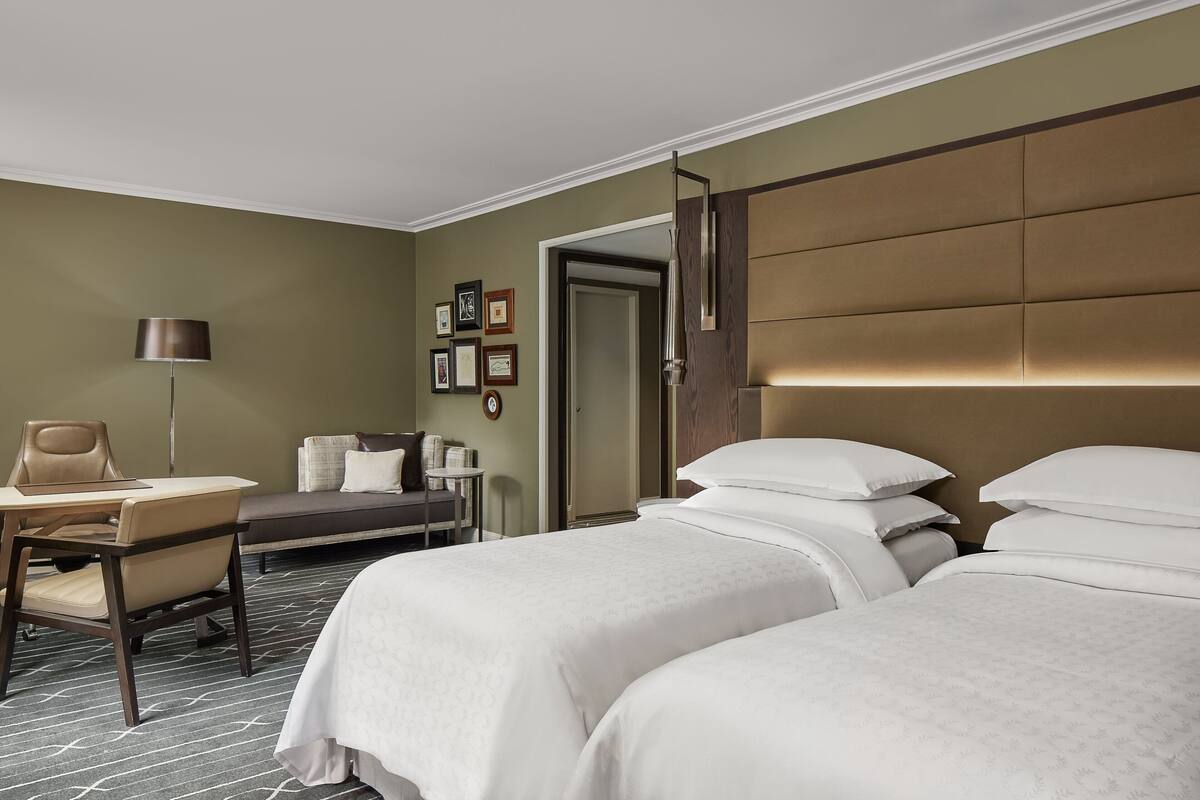 Een hotelkamer met twee bedden, een bureau, een stoel, een lamp en een bank.