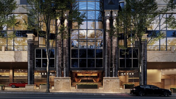 A hotel entrance with a glass facade, columns, and a red car parked in front.
