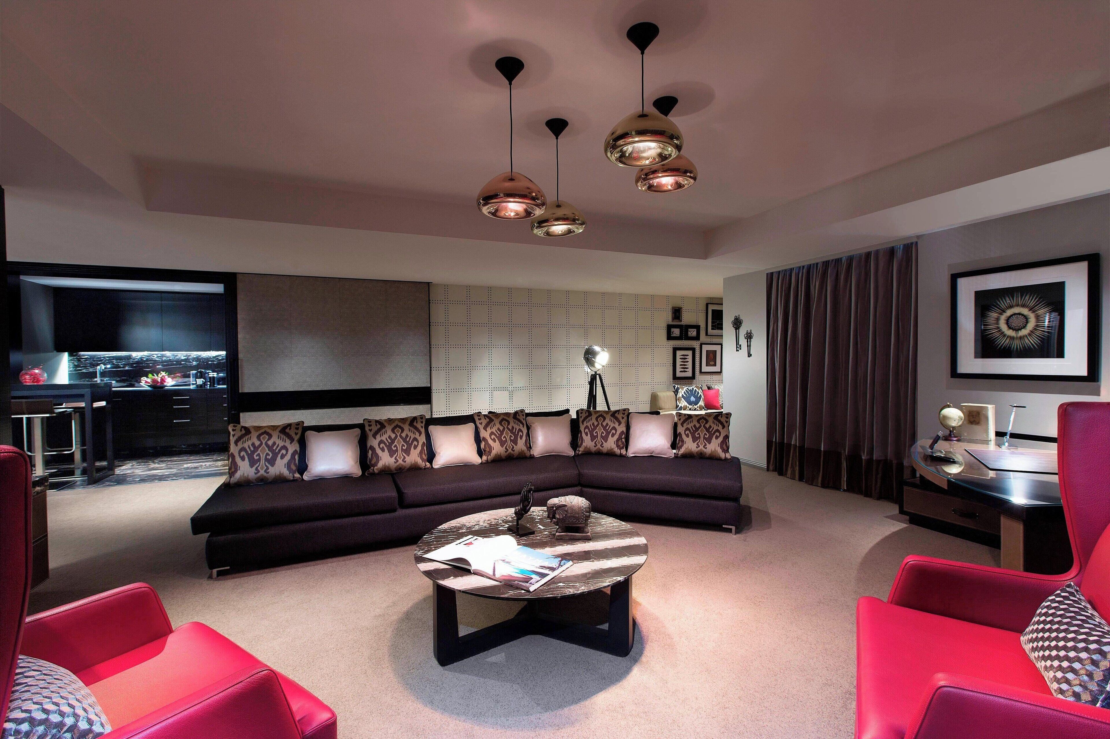 Uma sala de estar moderna com sofá de canto, poltronas vermelhas, mesa de centro e iluminação pendente.