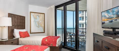 A hotel room with two beds, a TV, a map on the wall, and a balcony with a view of the sea.