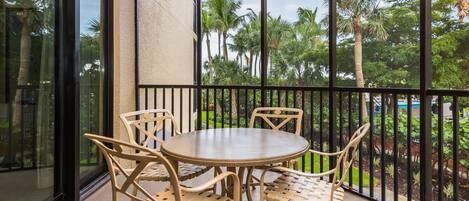 A balcony with a round table and four chairs, overlooking a garden with palm trees.