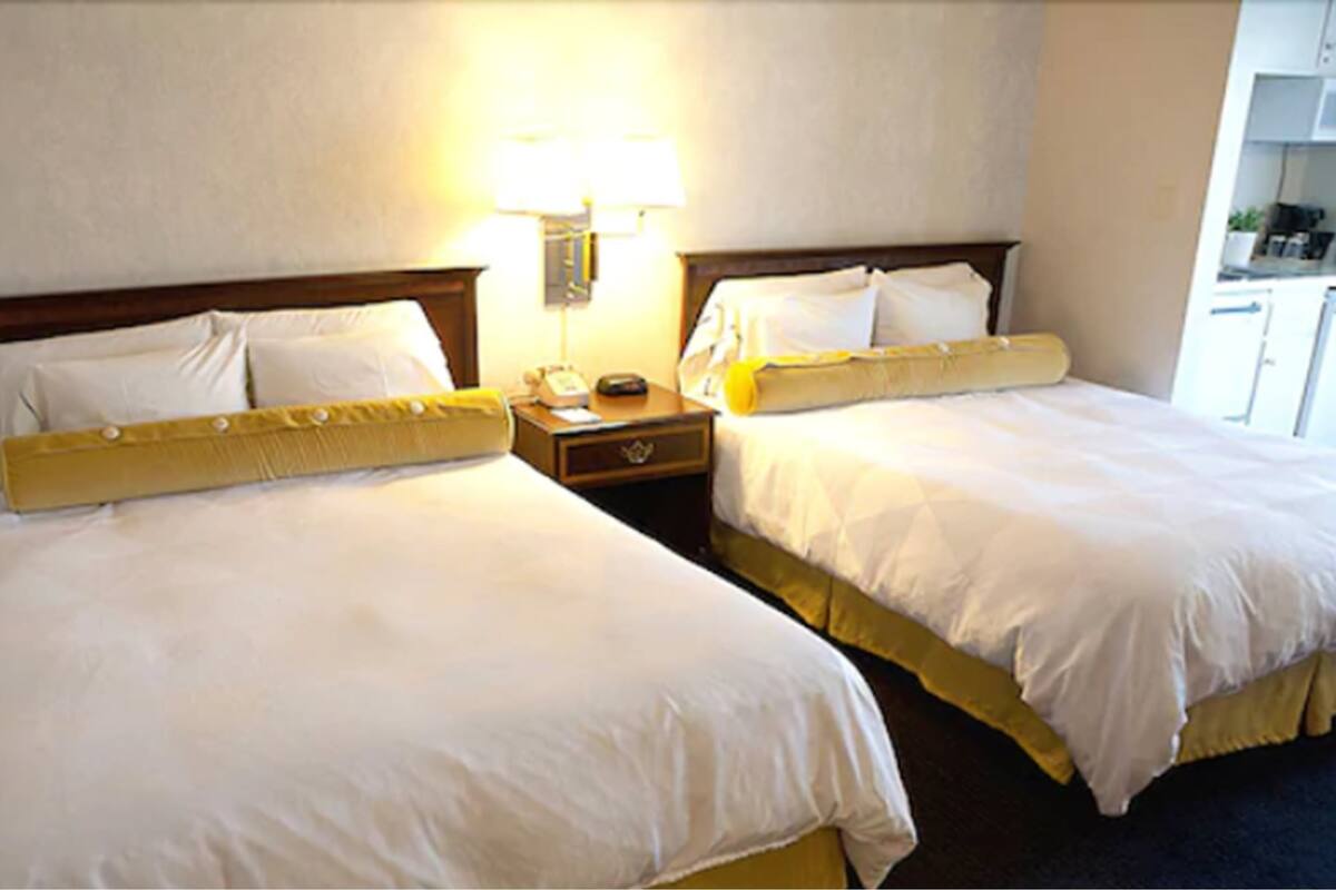 Une chambre d’hôtel avec deux lits, une table de chevet avec une lampe et une vue sur la cuisine.