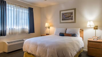 Habitación de hotel con una cama grande, dos lámparas de noche, un cuadro en la pared y una ventana con cortinas.