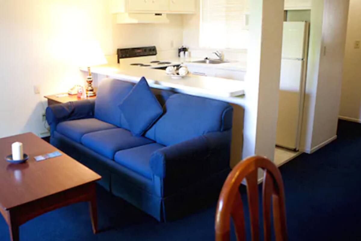 Un espace de vie compact comprenant un canapé bleu, une petite table en bois et un coin cuisine.