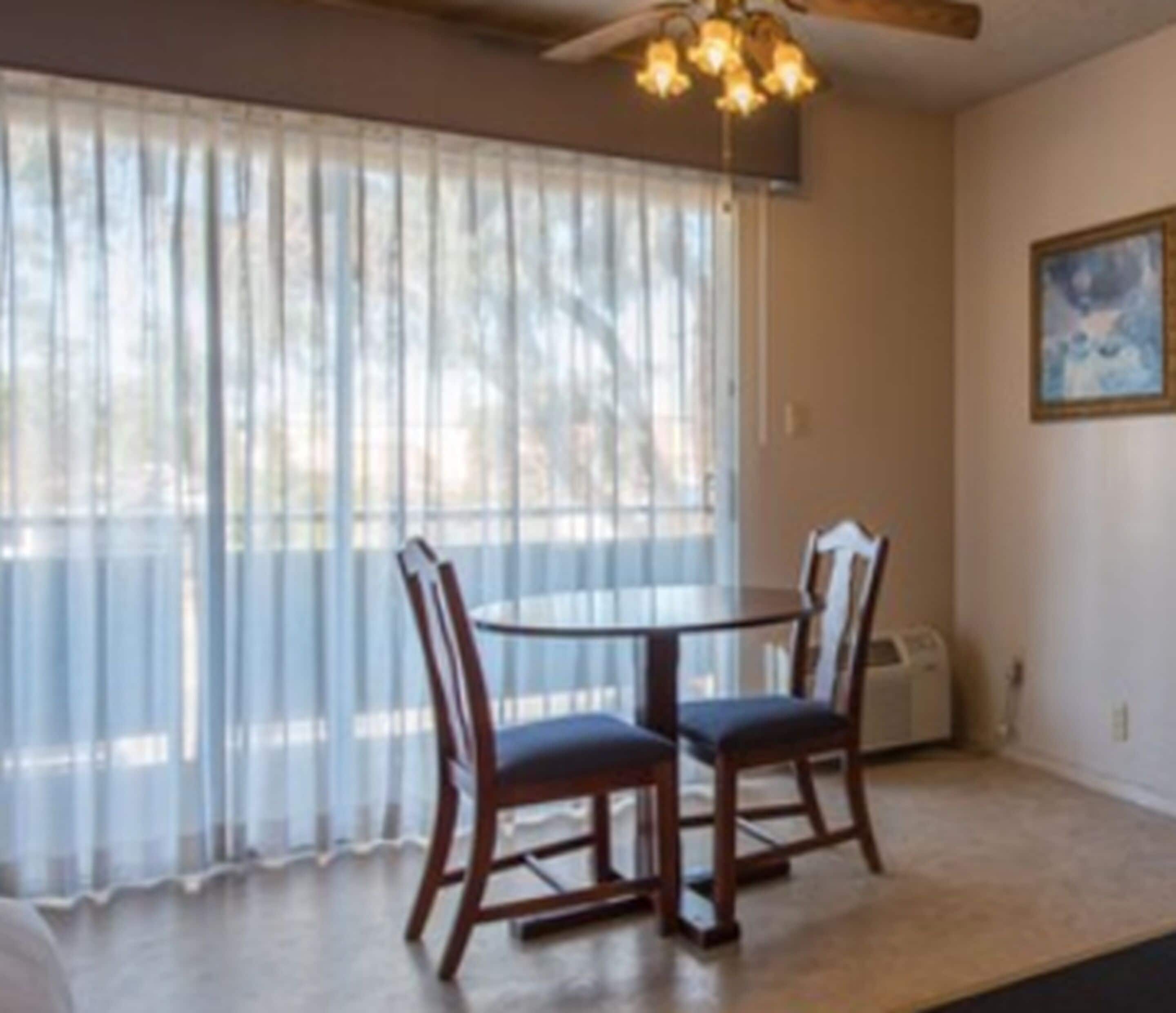 A dining area with a table and chairs, a ceiling fan, and a window with sheer curtains.