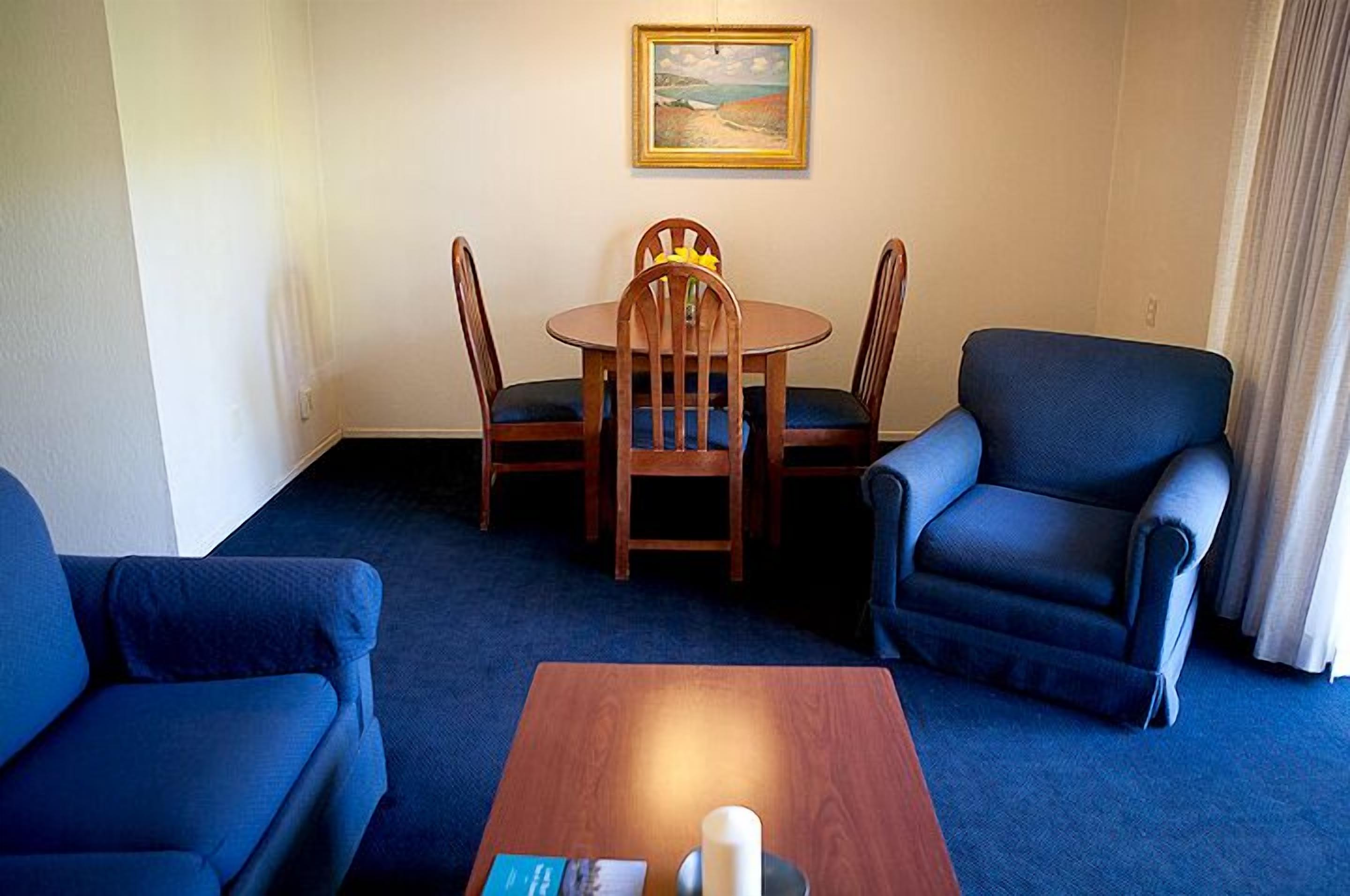 A room with a round wooden table and four chairs, a blue armchair, and a sofa.