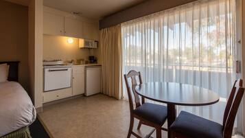 Habitación de hotel con cama, kitchenette, mesa de comedor con sillas y un ventanal con cortinas.