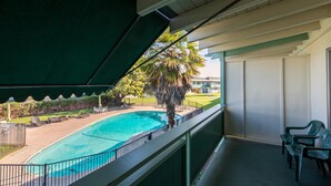 Un balcon donnant sur une piscine, un palmier et un bâtiment en arrière-plan.
