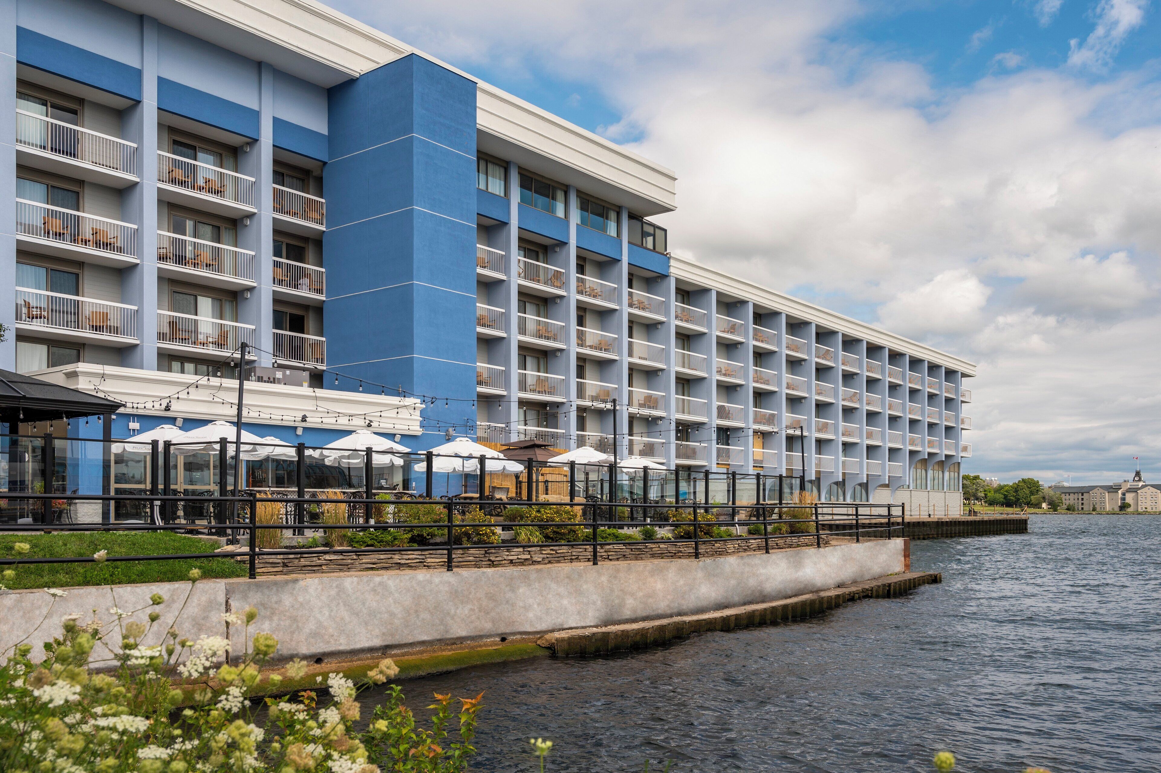 A hotel with multiple balconies, outdoor seating with umbrellas, and a waterfront view.